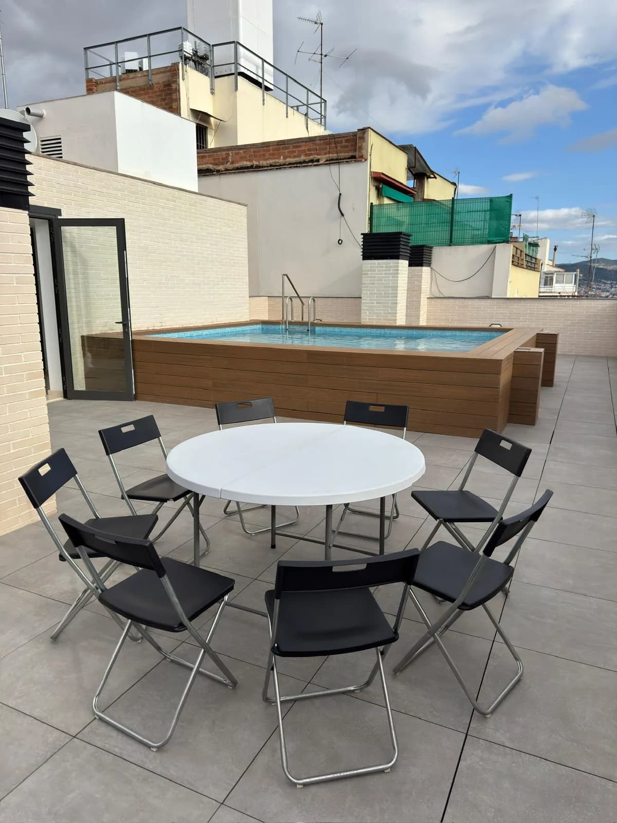 Taula rodona amb vuit cadires plegables negres en una terrassa amb piscina
