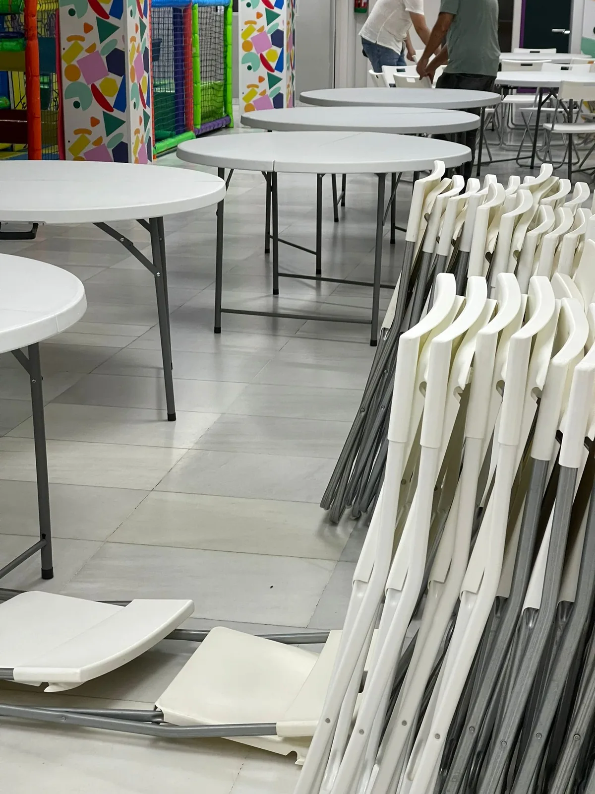 Muntatge de taules rodones i cadires plegables en un local infantil